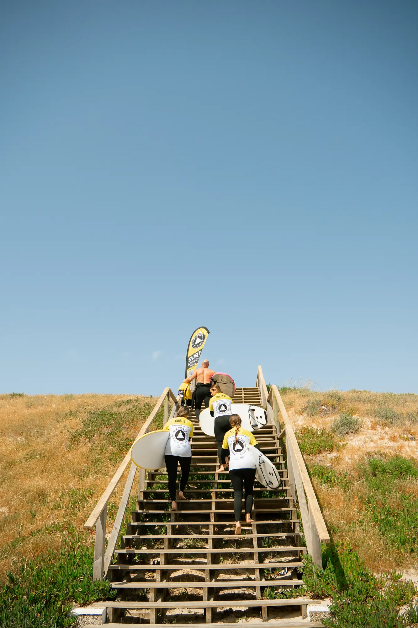 Surfer walking up the beach steps beneath a clear sky